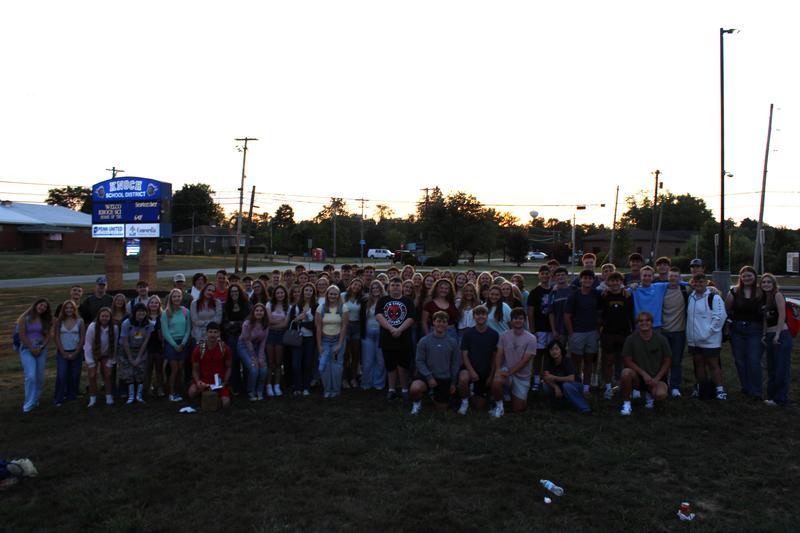 large group of students posing in front of a sunrise