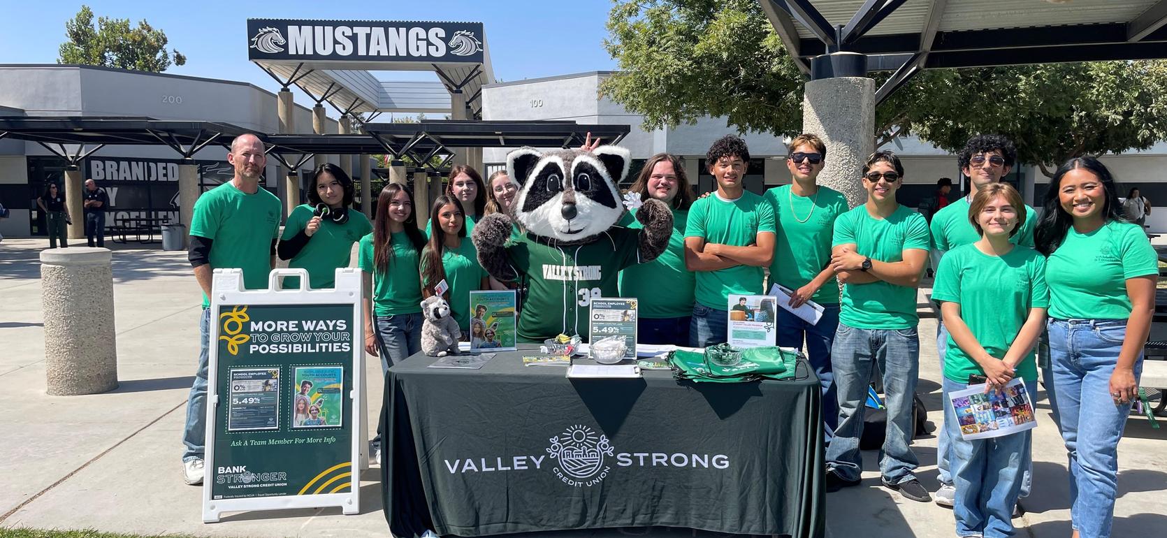 A group poses with a mascot at a school event, all wearing green shirts.