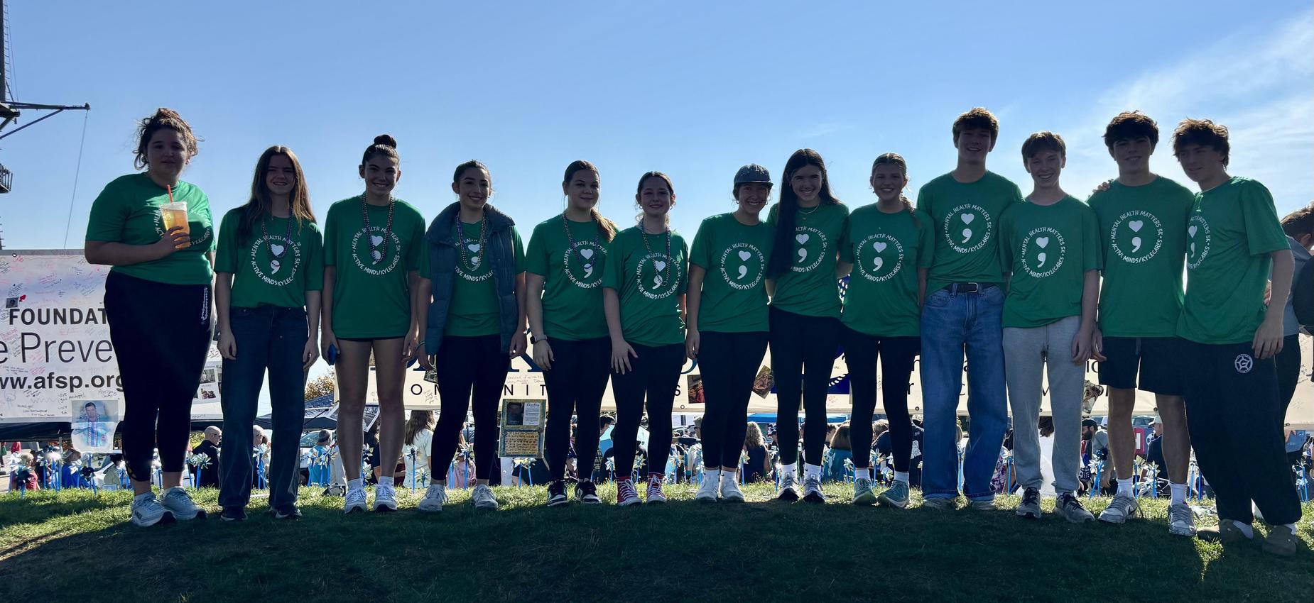 A group of eleven individuals wearing green shirts, standing outdoors with a blue sky.