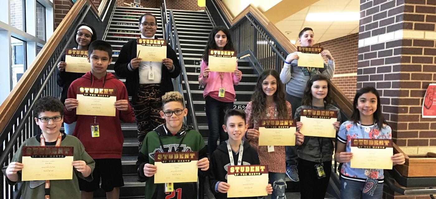 group of 11 students pose on steps with student of the month certificates