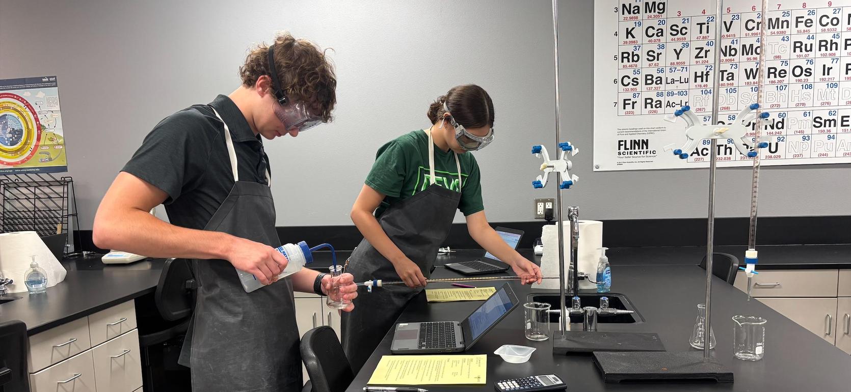 Two students conducting an experiment in a lab with various glassware and equipment.
