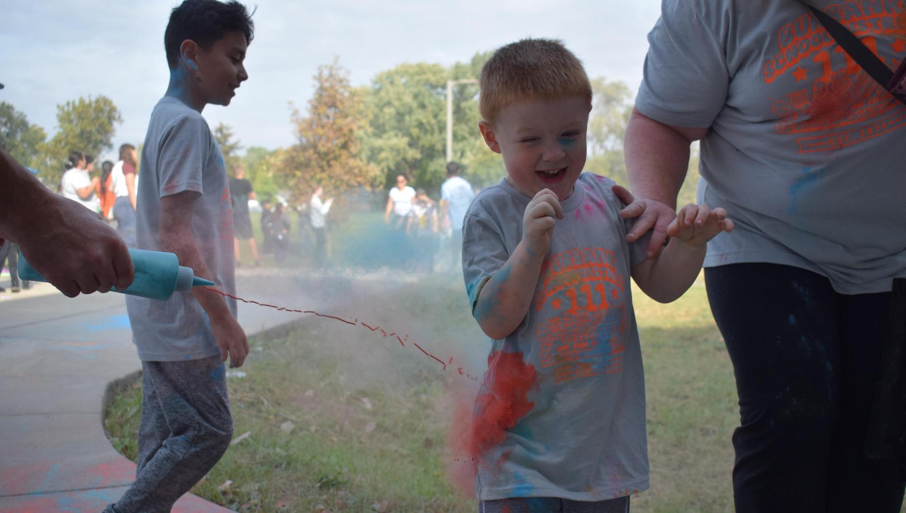 Child laughing while getting splashed with colorful powder paint at an outdoor event.