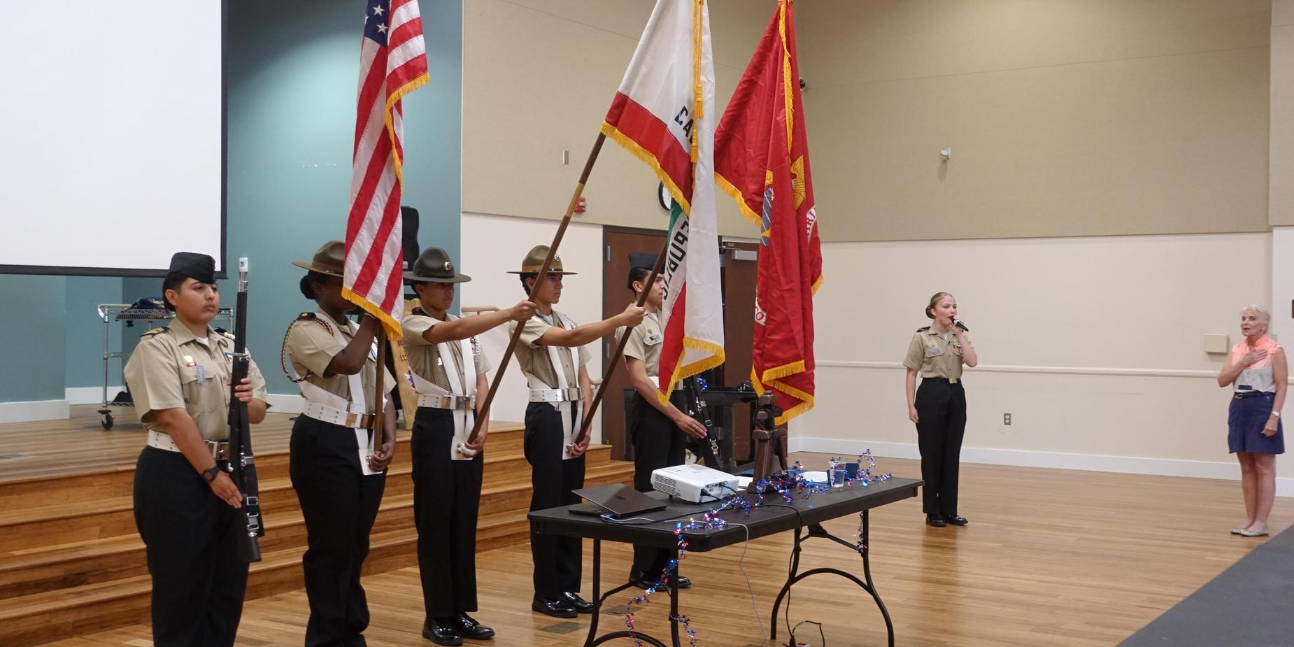 Color guard presenting flags at a formal event with an audience in attendance.