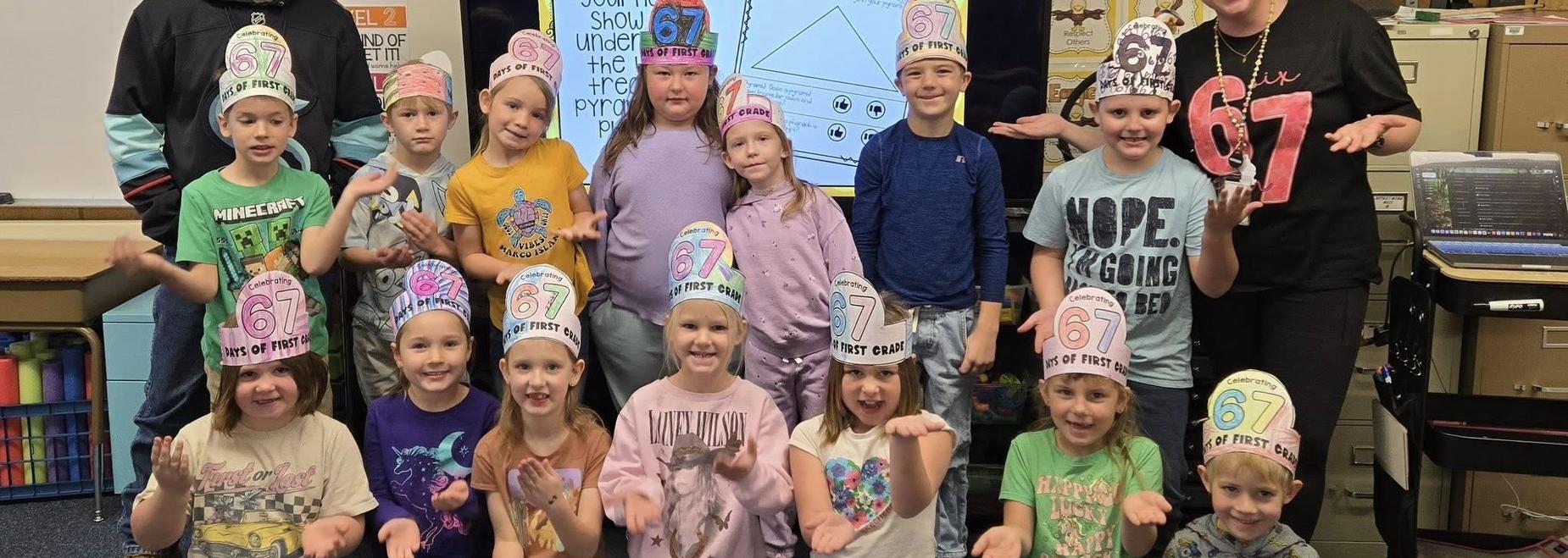 A group of children in colorful hats showing hand gestures, smiling together in a classroom.