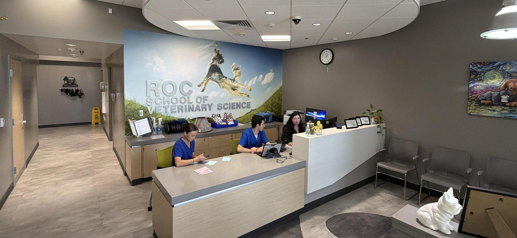 Veterinary school reception area with two staff members and a scenic mural.