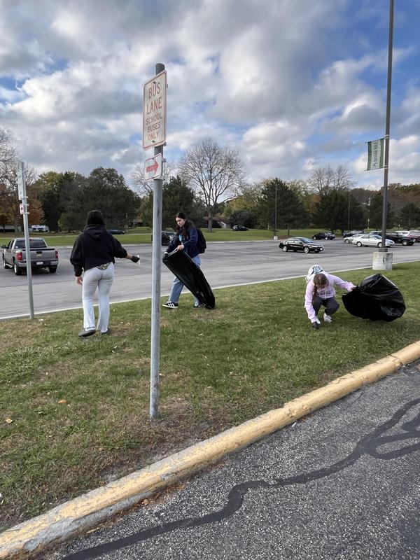 Group of volunteers picking up litter near a parking lot on a cloudy day.