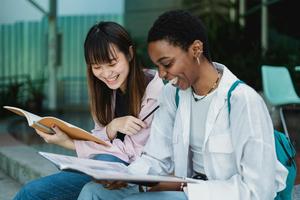 Two students seated on steps laugh while they study together.