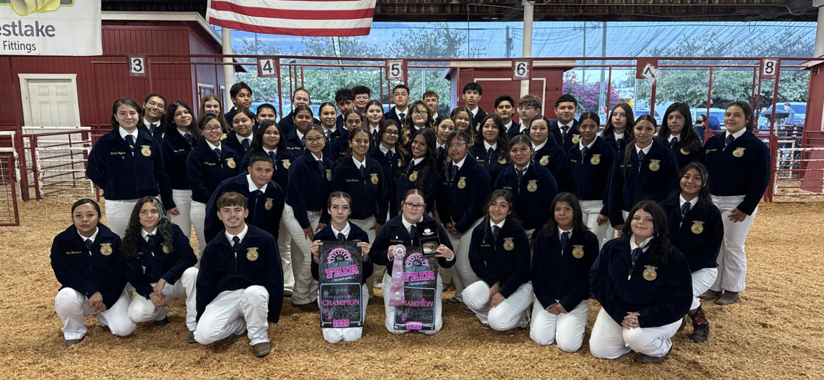A large group of students in navy jackets posing together in an indoor arena.