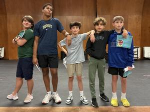 Image depicts five male students posing on the stage at QVMS in street clothes during rehearsals.