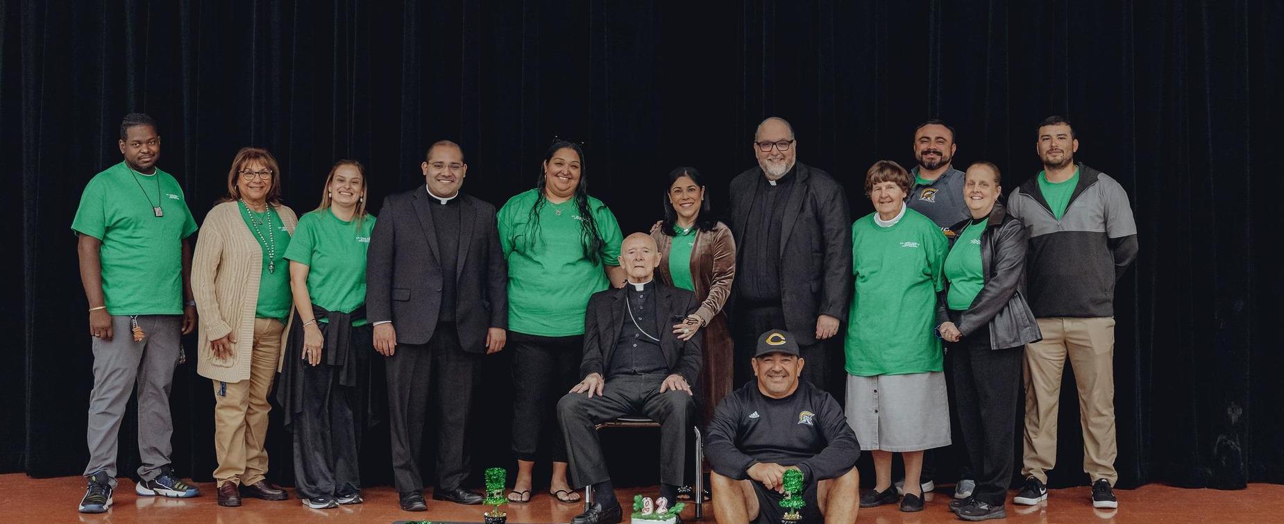 Group of people in green shirts, gathered for a photo on stage.