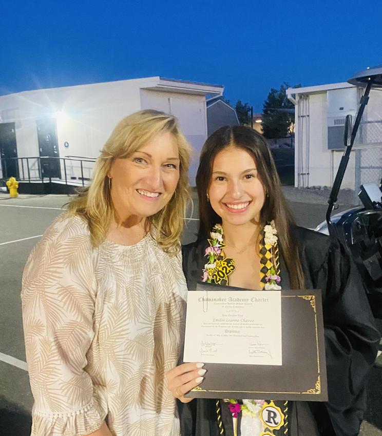 Two women smiling together, one holding a diploma, celebrating graduation.