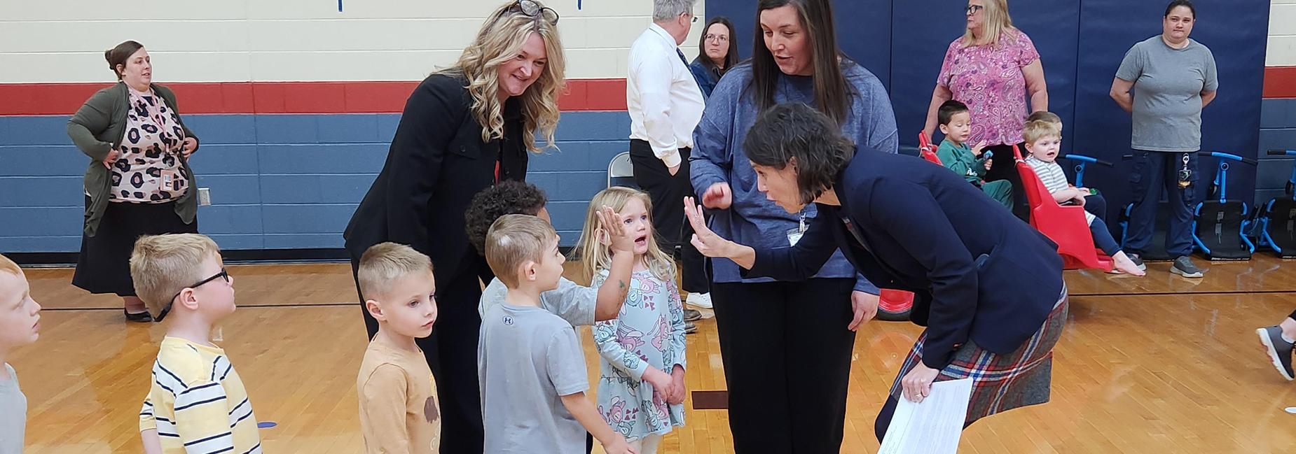 three adults bent over talking to pre-k students