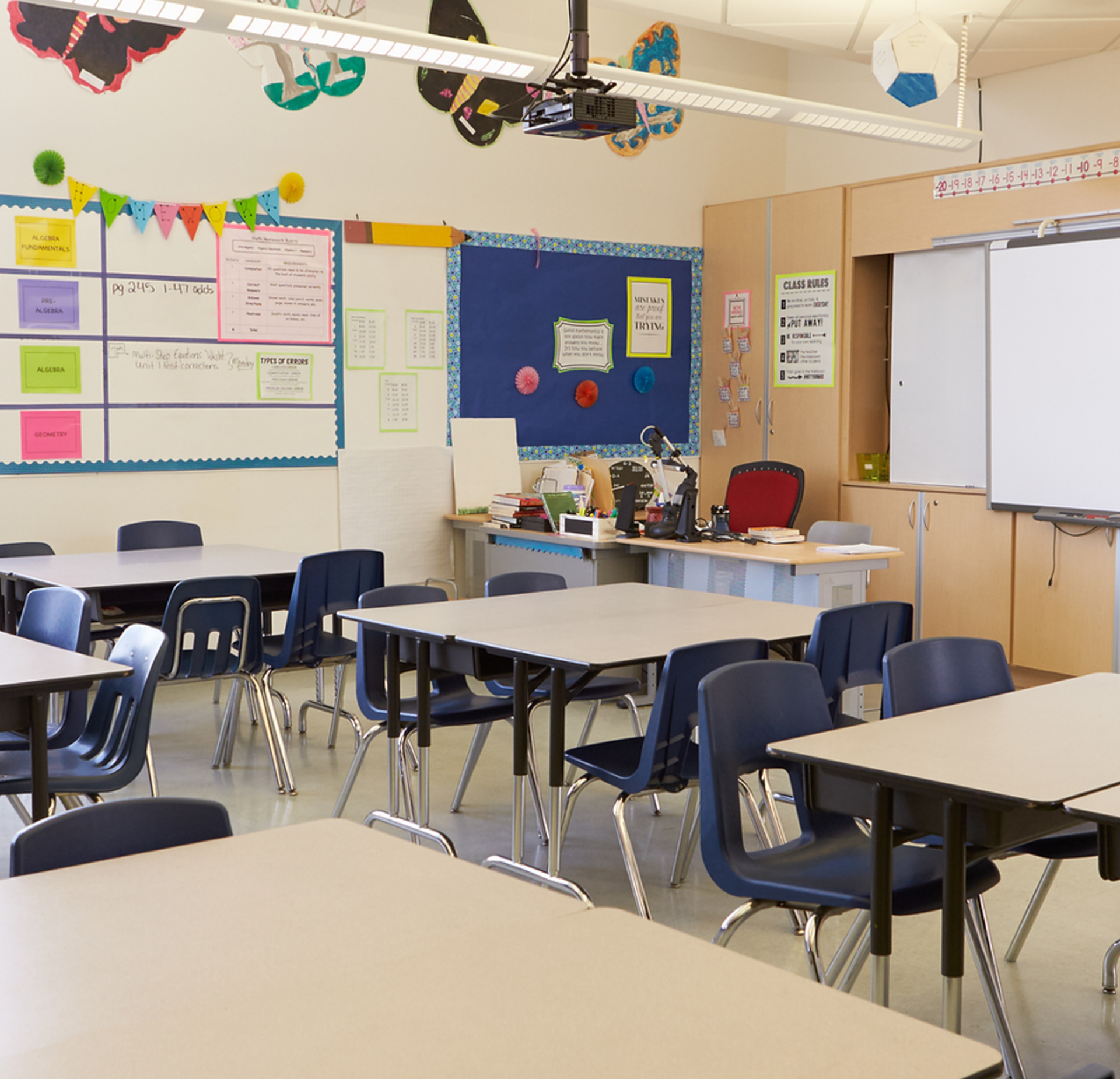 Empty classroom with desks, chairs, and a projector at the front.