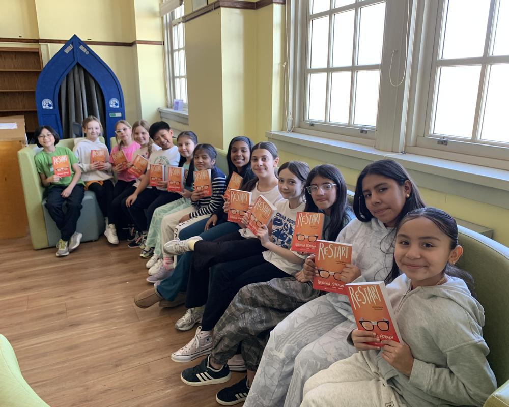 A group of students from reading club holding books, sitting in the library.