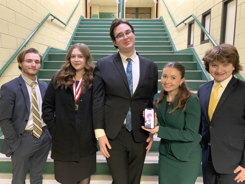 Group of five students dressed in formal attire posing on a school staircase.