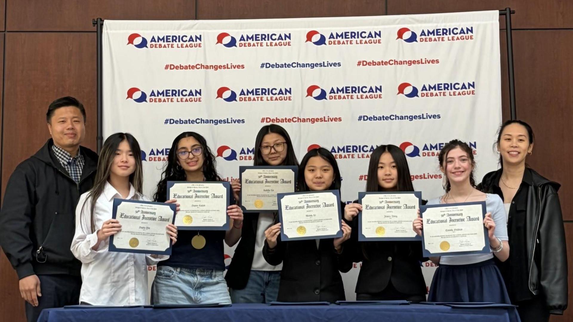 Group of six students holding certificates, posed in front of a banner.
