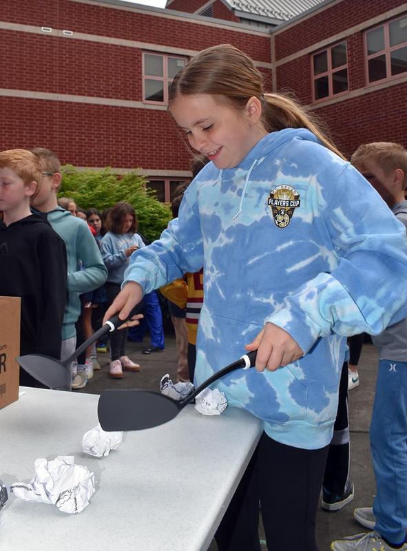 A girl uses two spatulas to dig into paper shreds in a box during an event.