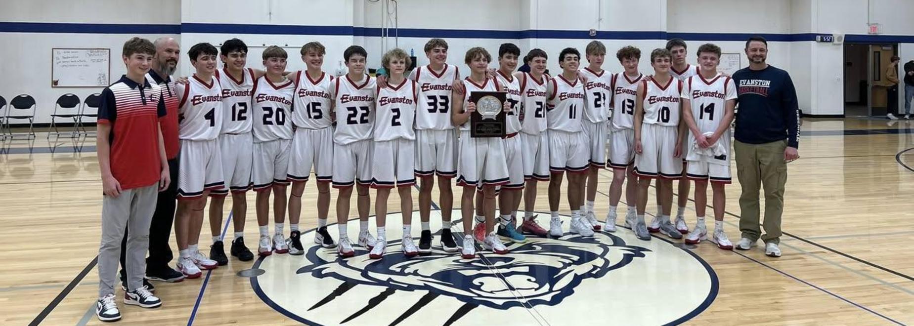 Team of young male basketball players celebrating with a trophy in a gymnasium.