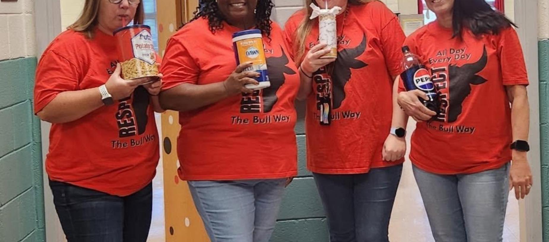 Four women in red shirts holding snacks and drinks in a school hallway.