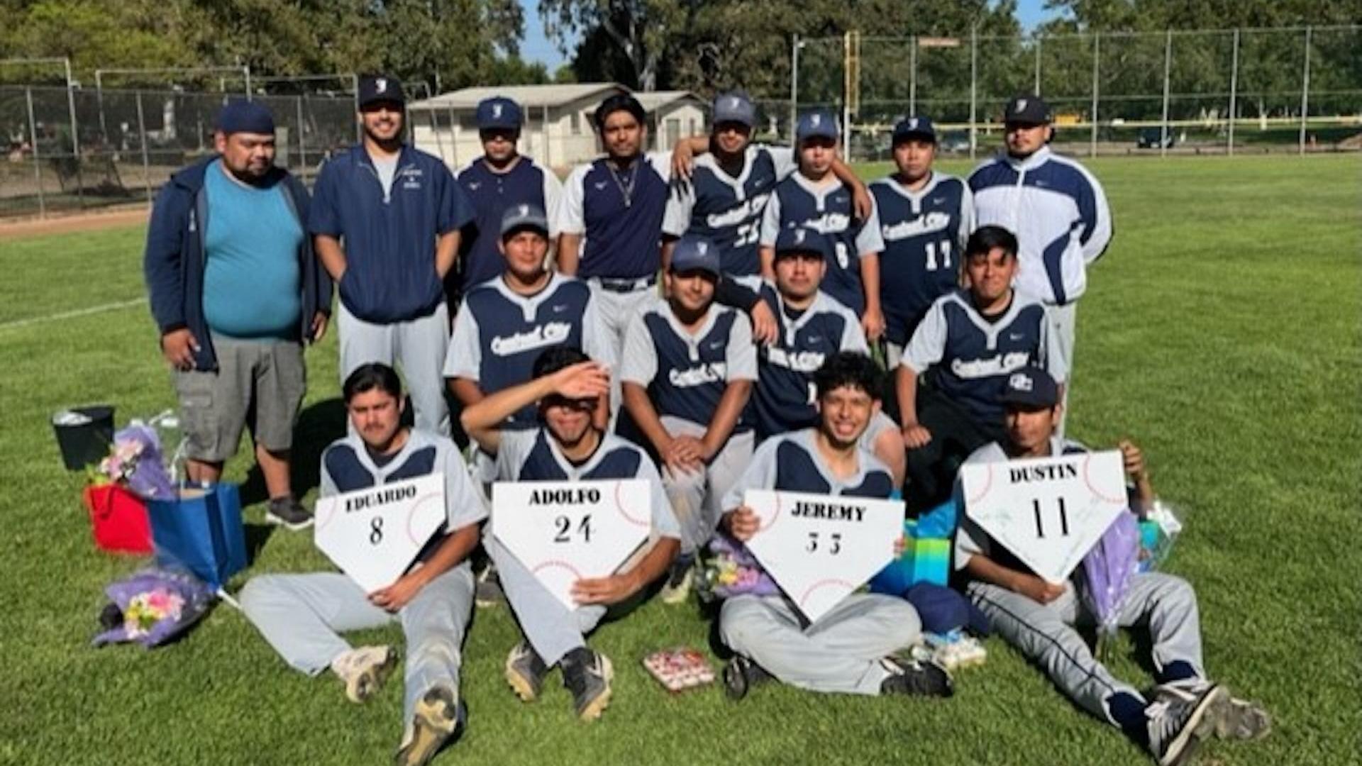 Group photo of a baseball team celebrating with flowers and signs on a field.
