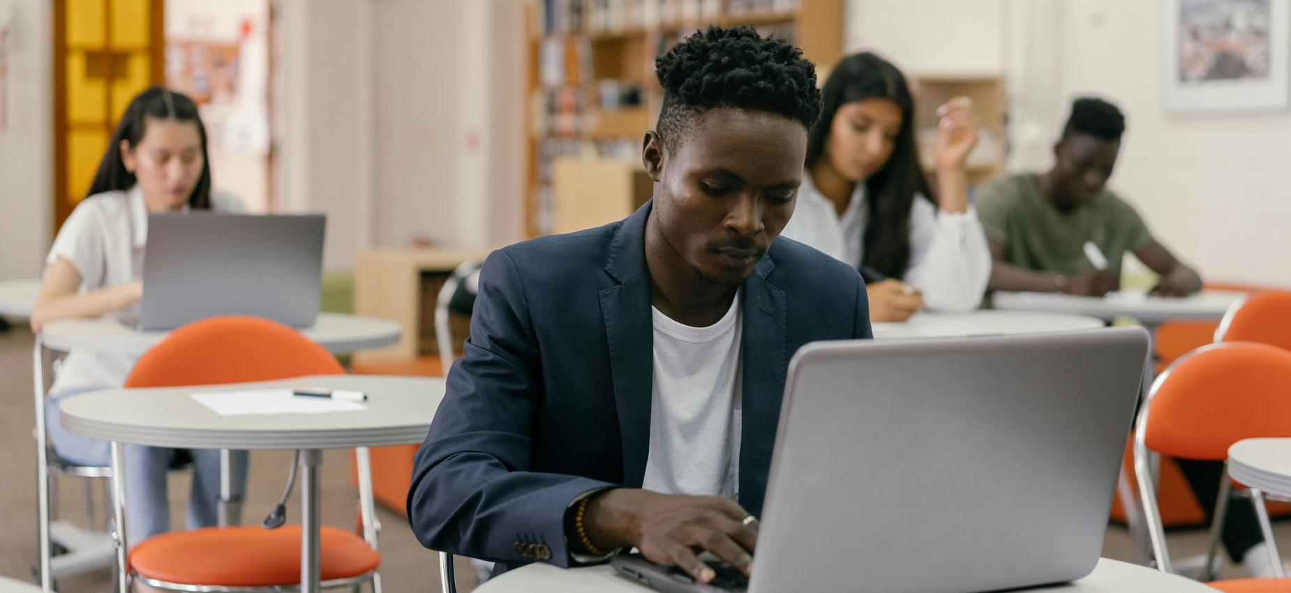 Student in a blazer focused on a laptop while classmates study.