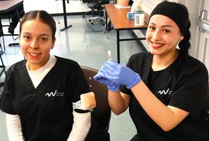 Two female Hispanic students in medical scrubs in the medical assistant classroom