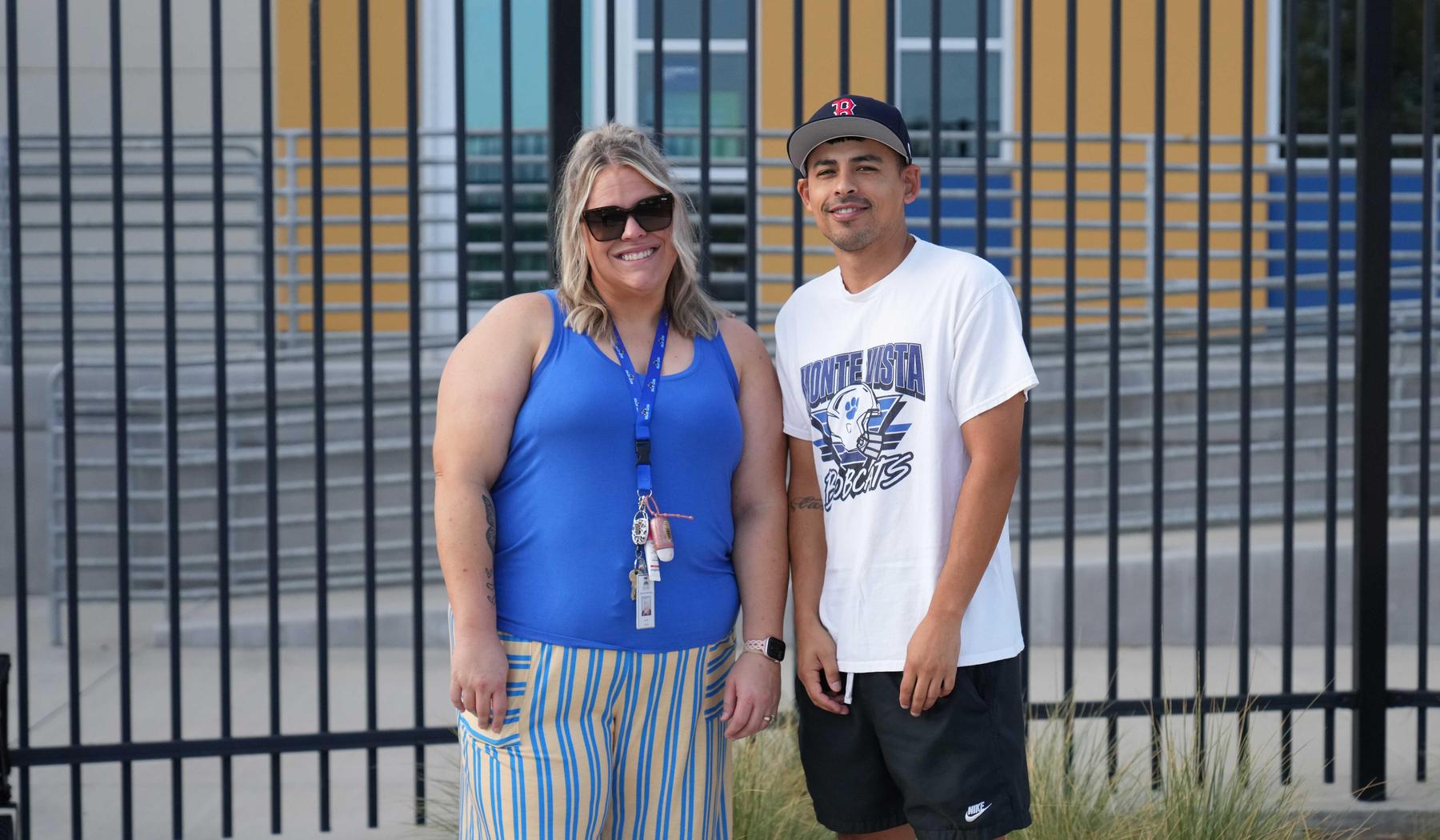 two staff members stand outside the fence to greet students