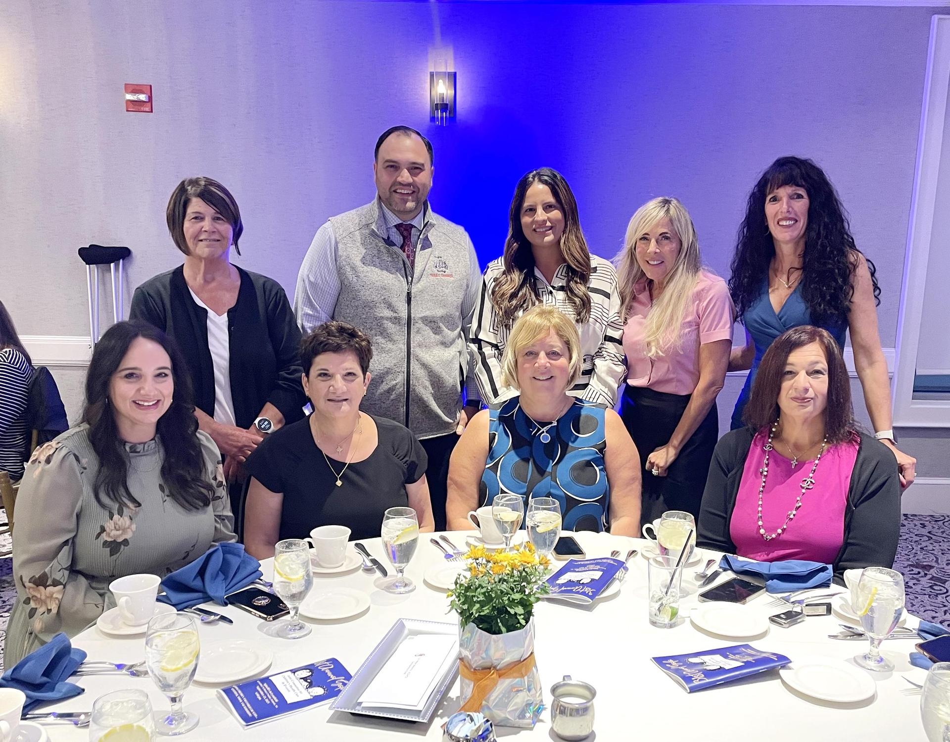 A group of nine colleagues smiling together at a formal dining table.