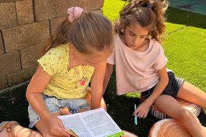 Two girls sit in a courtyard on the ground and work on an assignment