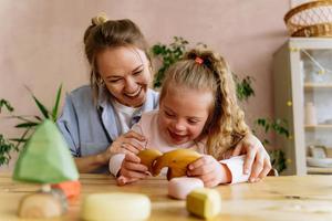 A smiling adult sits with a child playing with wooden toys.