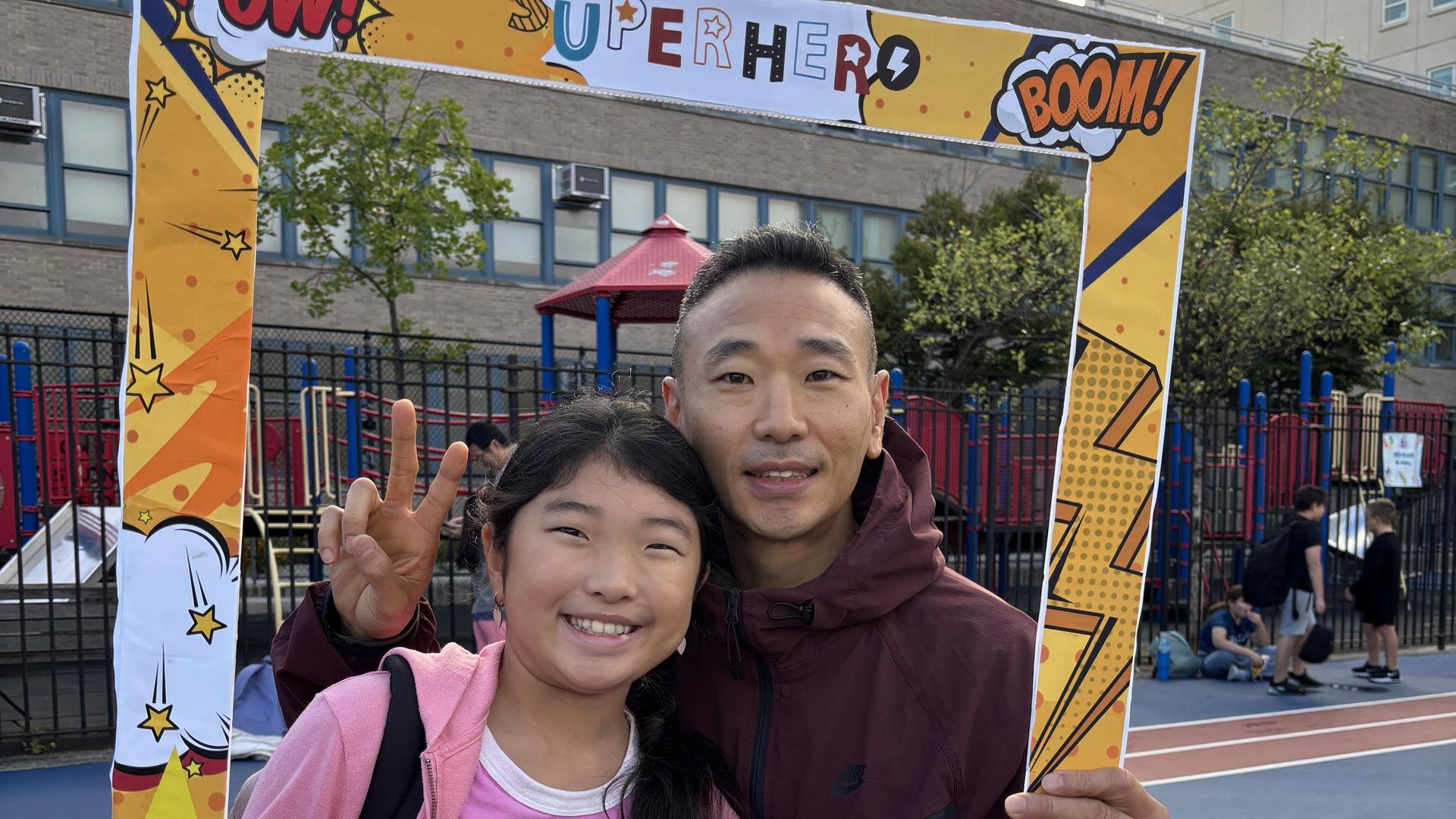 A man and a girl smiling together inside a fun photo frame outdoors.