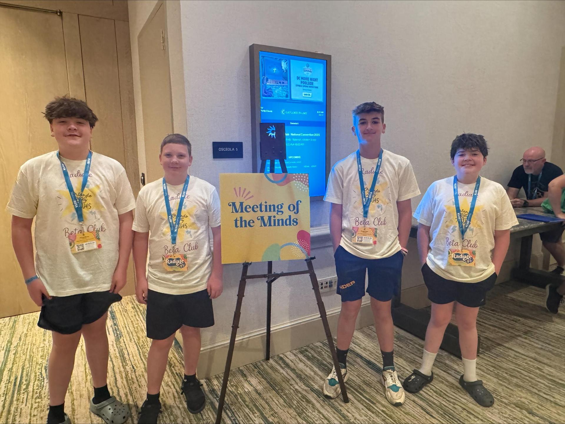 Four boys with Meeting of the Minds sign in hotel. 