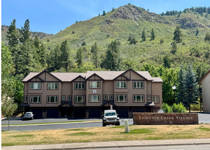 A brown apartment building with mountains in the background and a sign in front that says Lightner Creek Village.