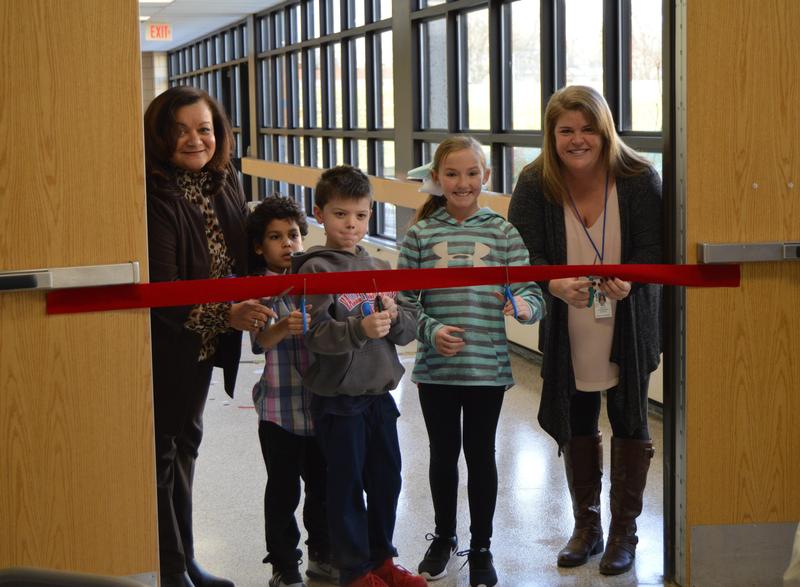 Valley principal Mrs. Toller and 2 boys and a girl along with Special Education teacher Ms. Hill have scissors on a red ribbon prior to cutting it.