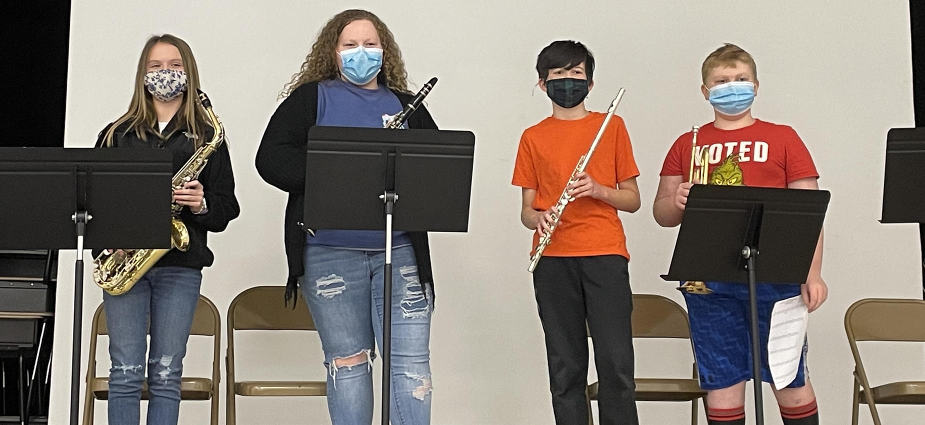 Four students stand on a stage with instruments.