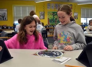 Girls laugh while examining a game board at a table.