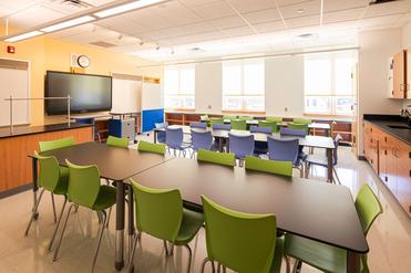 A modern classroom with green and blue chairs arranged around tables.