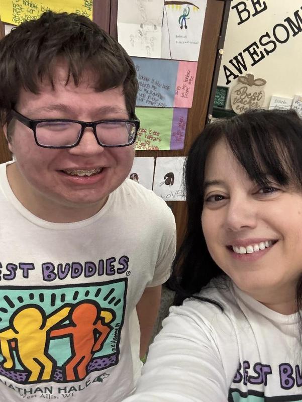 Two individuals smiling for a selfie wearing matching t-shirts in a colorful environment.