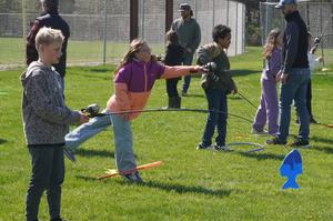 Students practice casting a fishing pole to catch plastic fish in the grass.