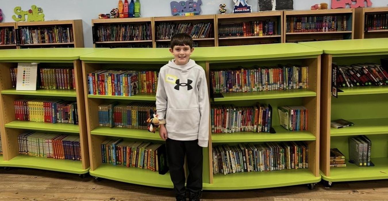 A boy stands in a colorful library with bookshelves filled with books.