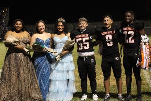 Group of football players and homecoming queens posing together on the field.