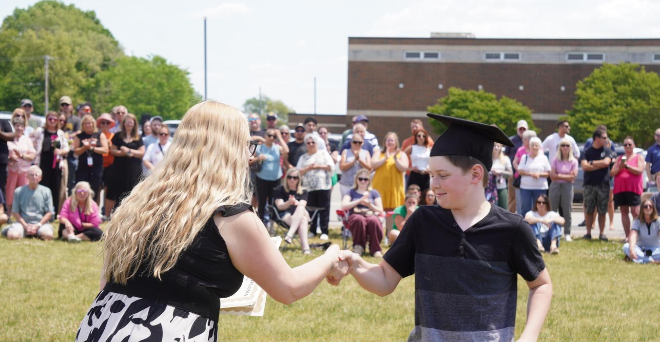 Graduation ceremony with a child receiving a diploma and applauding crowd.