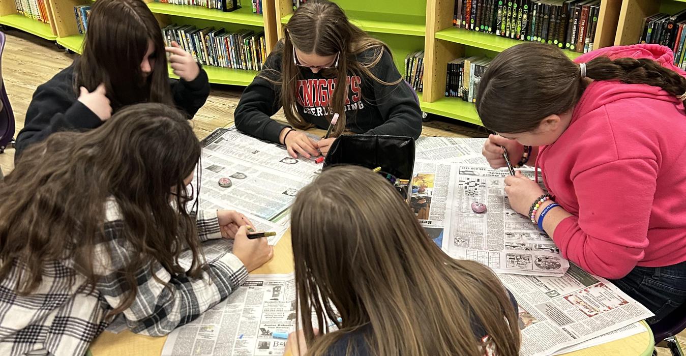 Group of girls coloring stones on newspaper-covered table in a classroom.