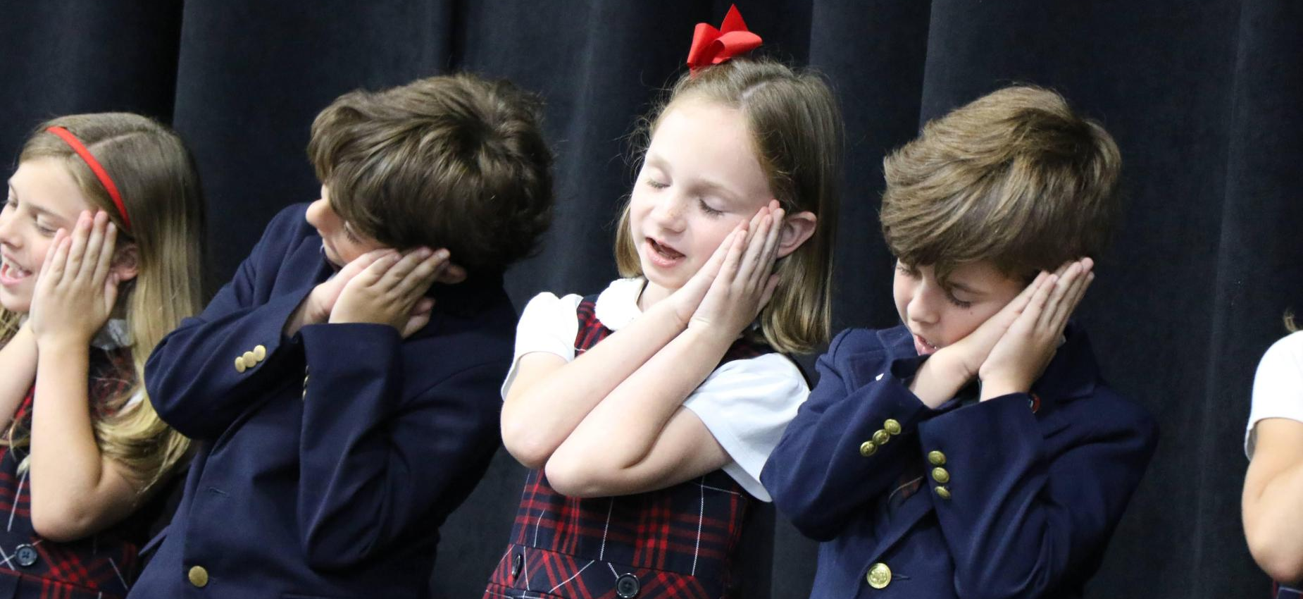 Four children in formal attire performing a turning gesture with smiles.