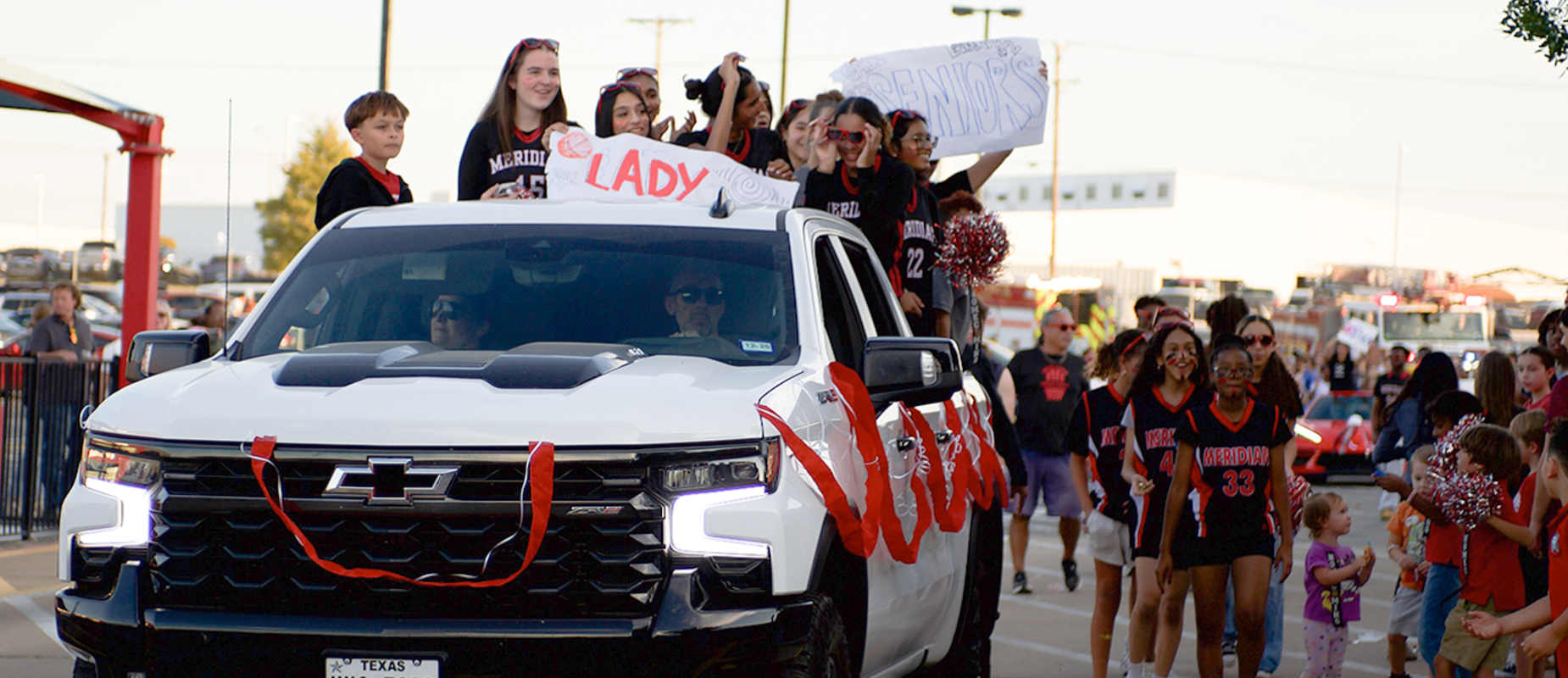 Homecoming parade with students in sports uniforms and younger students cheering them on