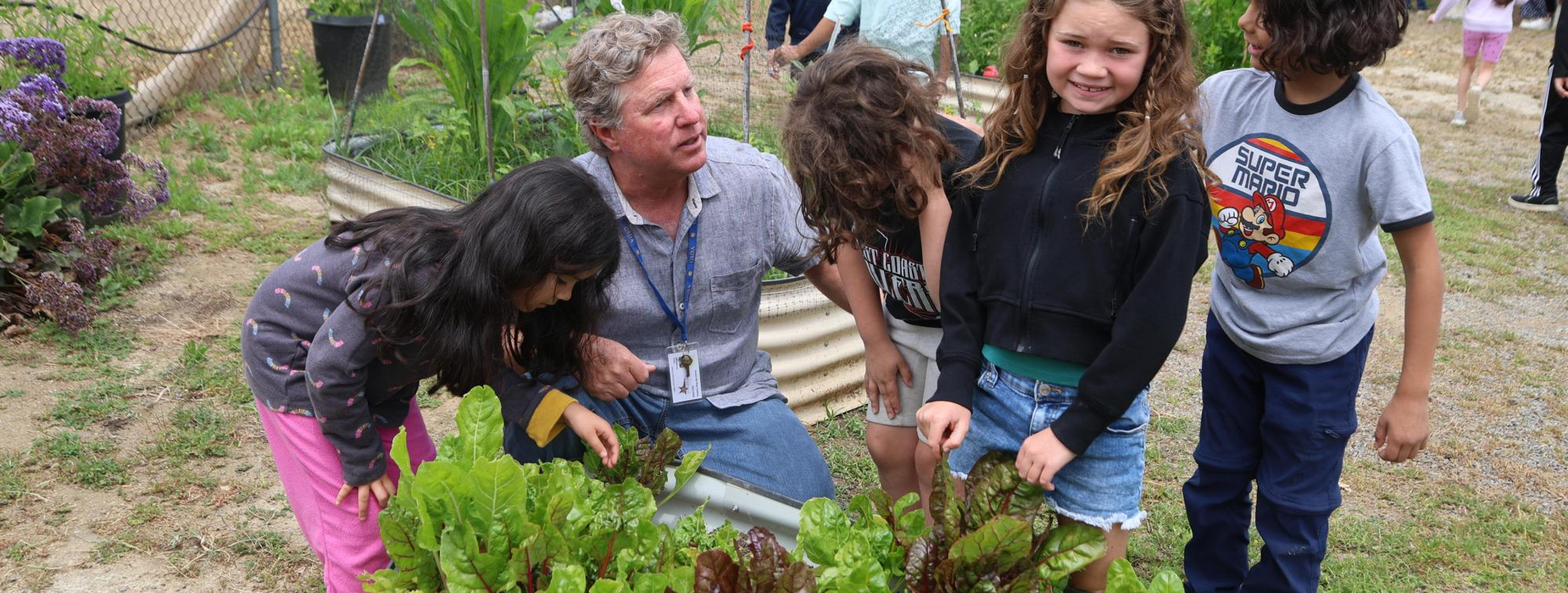 Group of children and a man gardening together with plants.
