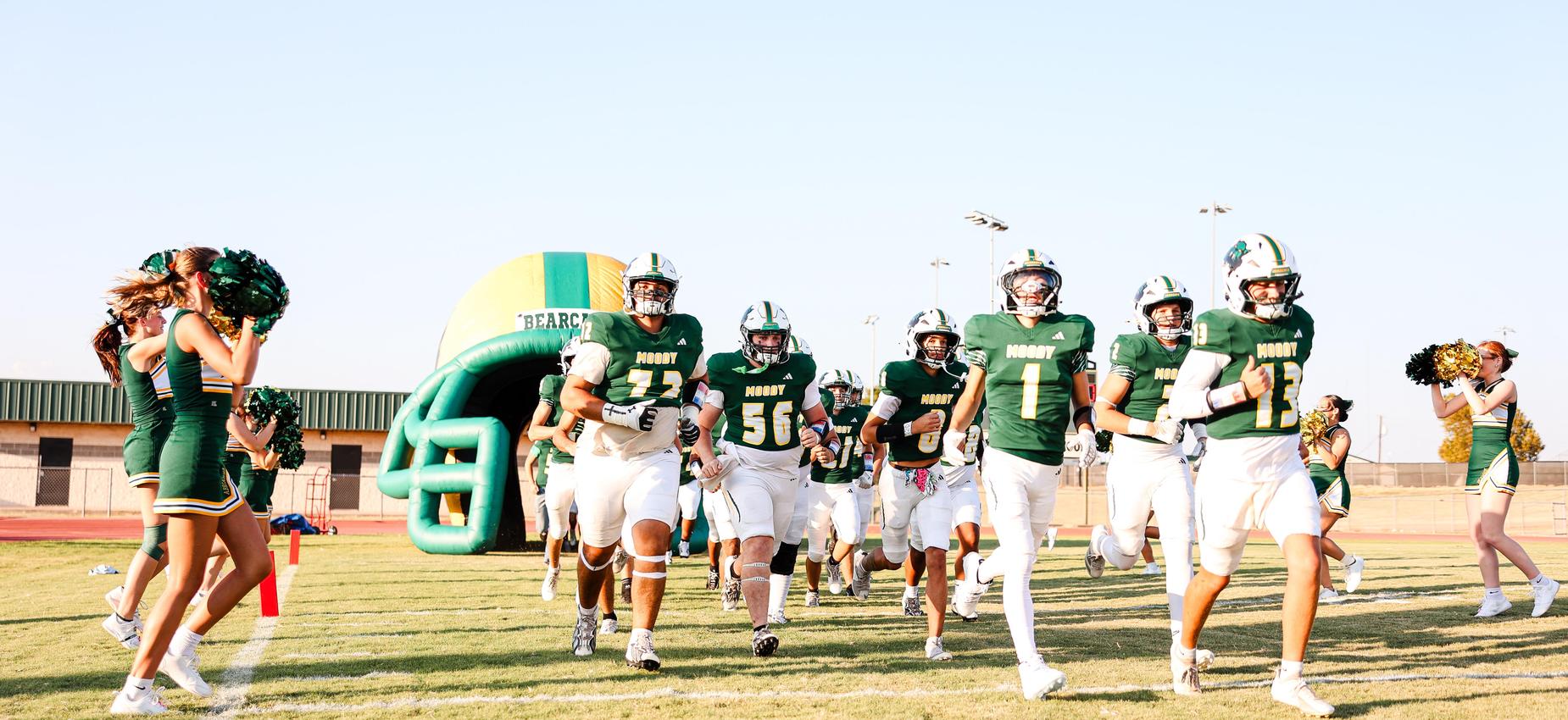 Football players running onto the field with cheerleaders in the background.