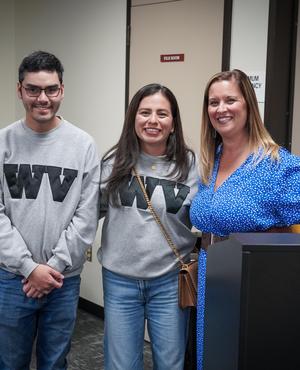 Two students and a woman pose together, all wearing matching sweatshirts.