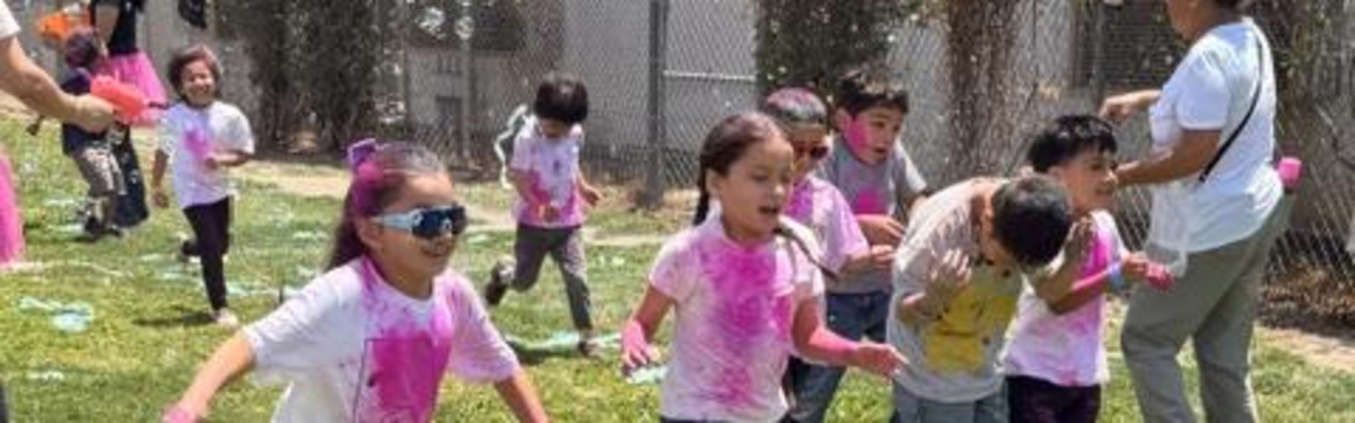 Children running on grass, adorned with colorful splashes of paint.