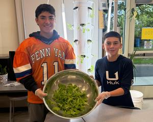 Two students hold a large metal bowl filled with harvested lettuce in front of an indoor Grow Tower.